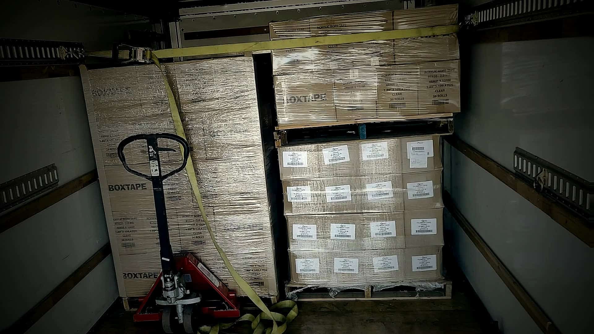 Red pallet jack beside strapped BOXTAPE pallets inside a delivery truck